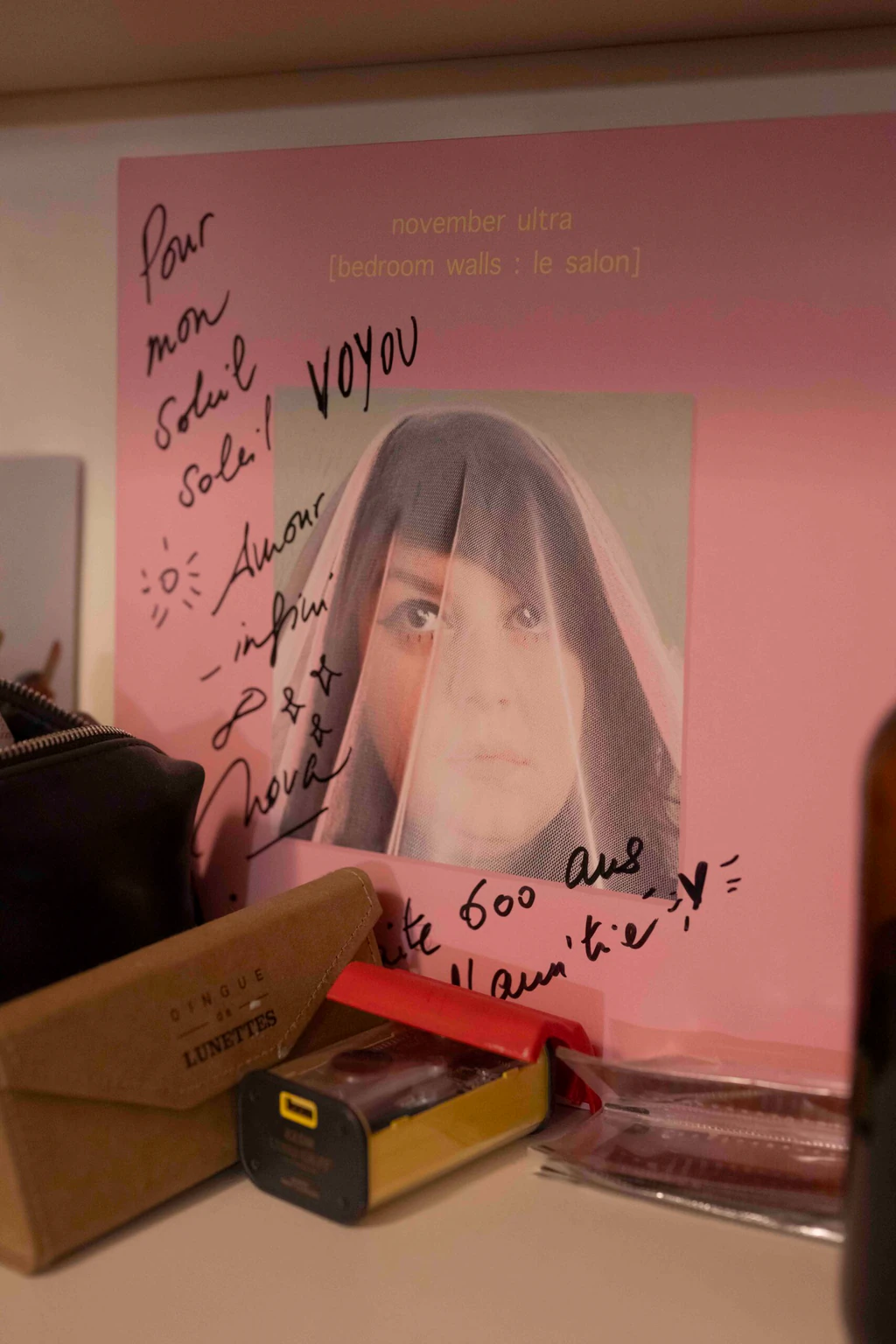 Pochette de disque de November Ultra dédicacée « pour mon Soleil, Amour infini, Voyou », posée sur une étagère avec des lunettes et une boîte de pellicules photo